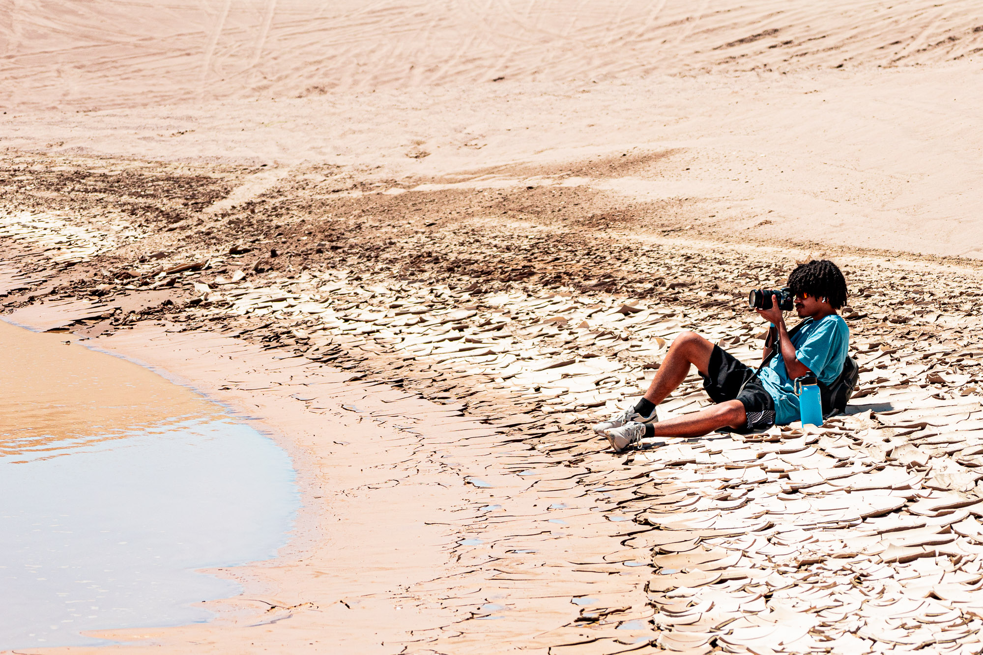 Roby Davis photographing on cracked desert earth beside still water